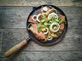 Fried meat on the iron plate with rustic wooden background. Flat lay.