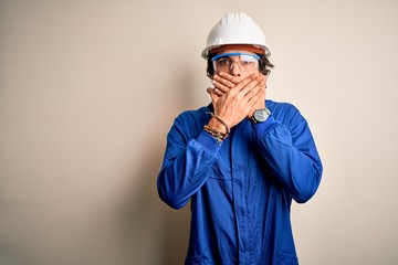 Young constructor man wearing uniform and security helmet over isolated white background shocked...