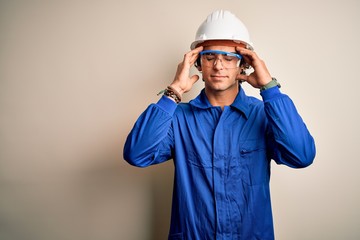 Young constructor man wearing uniform and security helmet over isolated white background with hand on head for pain in head because stress. Suffering migraine.