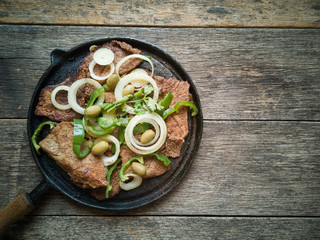 Fried meat on the iron plate with rustic wooden background. Flat lay.