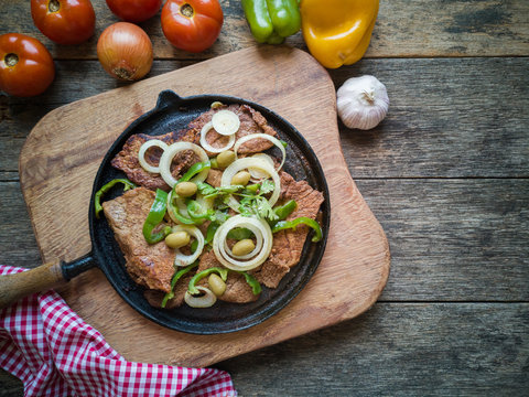 Fried meat on the iron plate with rustic wooden background. Flat lay.