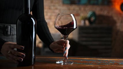 Woman tasting and drinking red wine from wine from elegant wine glass at home in a cosy dark room.