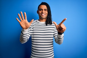 Young handsome african american afro man with dreadlocks wearing casual striped sweater showing and pointing up with fingers number seven while smiling confident and happy.