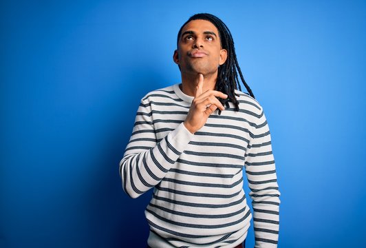 Young handsome african american afro man with dreadlocks wearing casual striped sweater Thinking concentrated about doubt with finger on chin and looking up wondering