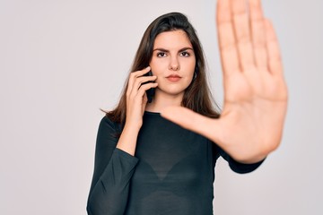 Fototapeta premium Young beautiful woman having a conversation talking on smartphone ove isolated background with open hand doing stop sign with serious and confident expression, defense gesture