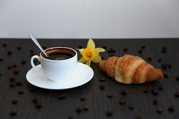 Morning coffee, spilled coffee beans, two cups of coffee, wooden table, flowers, daffodils, croissants, breakfast