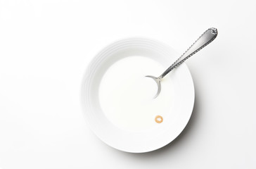 Flat lay white cereal bowl with spoon and one piece of cereal floating in the milk. High Key still life with copy space.