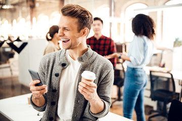 Happy young man holding cellphone and coffee cup