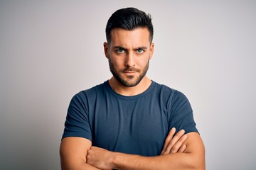 Young handsome man wearing casual t-shirt standing over isolated white background skeptic and nervous, disapproving expression on face with crossed arms. Negative person.