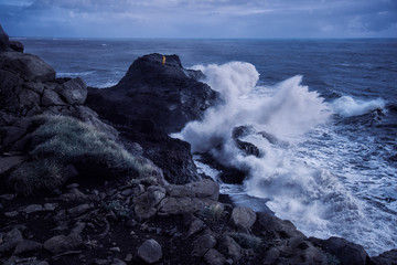 man in yellow raincoat at edge of cliff with huge waves on stormy day