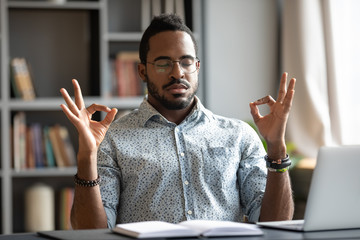Calm African American man sit at desk meditating relieving negative emotions breathing fresh air, relaxed biracial male distracted from work practice yoga with mudra hands, stress free concept - obrazy, fototapety, plakaty