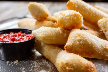 A closeup view of a silver pan of breadsticks and a cup of marinara sauce, in a restaurant or kitchen setting.