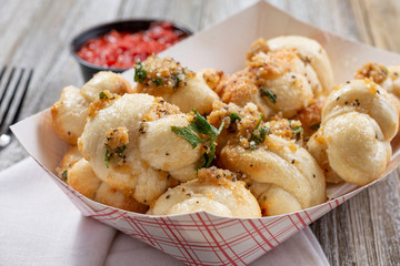 A closeup view of an appetizer container of garlic knots, in a restaurant or kitchen setting.