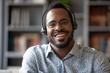 Head shot portrait of smiling African American male call center agent in glasses wireless headset,...