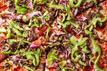 A top down view of a veggie and meat pizza pie in a restaurant or kitchen setting, as a background.
