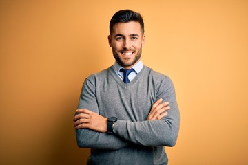 Young handsome businessman wearing elegant sweater and tie over yellow background happy face...