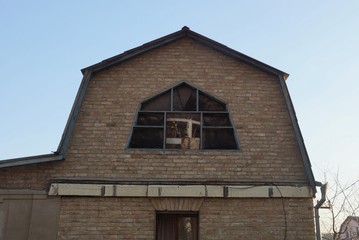 the attic of a rural private house of brown bricks with one large window against a blue sky