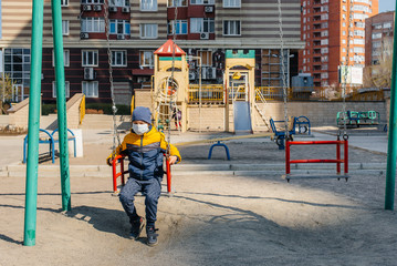 Fototapeta na wymiar A small boy in a mask walks on the Playground during the quarantine. Stay at home