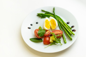 Boiled poached egg, cherry tomatoes, mix salad and asparagus on a white plate on an isolated white background. Healthy Diet Food Concept