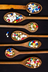 Obraz premium Assorted pharmaceutical medicine pills, tablets and capsules on wooden spoon on black background