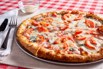 A view of a rustic margherita style pizza pie, in a restaurant or kitchen setting.