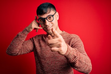Young handsome hispanic man wearing nerd glasses over red background smiling doing talking on the...