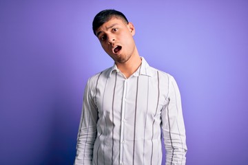 Young handsome hispanic man wearing elegant business shirt standing over purple background In shock face, looking skeptical and sarcastic, surprised with open mouth