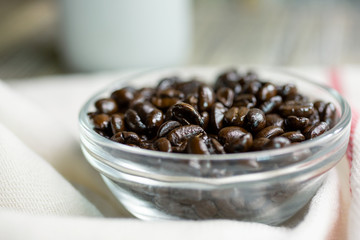 A closeup view of a glass condiment bowl of dark roasted coffee beans.