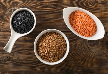 Different assorted lentils mix with red, brown and black beluga lentils in white bowls on brown wooden table background top view flat lay from above