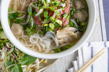 A top down view of a large bowl of pho with a variety of meat inside, in a restaurant or kitchen setting.