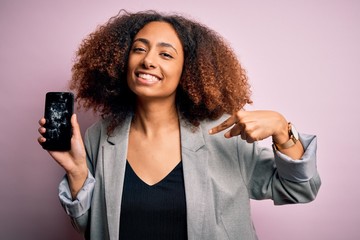 Young african american woman with afro hair holding cracked and broken smartphone screen with surprise face pointing finger to himself