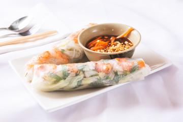 A view of a plate of spring rolls and peanut dipping sauce, in a restaurant or kitchen setting.