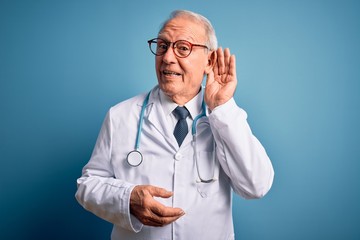 Senior grey haired doctor man wearing stethoscope and medical coat over blue background smiling...