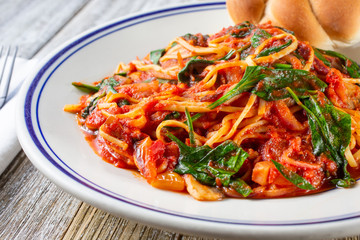 A closeup view of a bowl of spinach and tomato pasta, in a restaurant or kitchen setting.