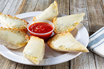 A view of a plate of cheesy garlic bread, with marinara sauce, in a restaurant or kitchen setting.