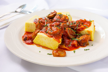 A view of a plate of polenta and sausage, in a restaurant or kitchen setting.