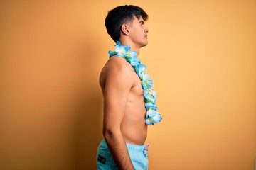 Young handsome tourist man on vacation wearing swimwear and hawaiian lei flowers looking to side,...