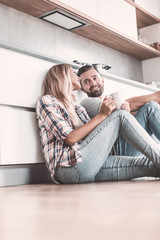young couple drinking coffee sitting on the kitchen floor