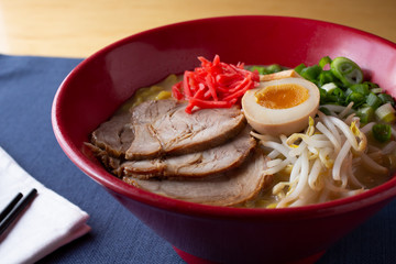 A closeup view of a bowl of Japanese tonkatsu white ramen, in a restaurant or kitchen setting.
