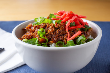 A closeup view of a Japanese rice beef bowl, in a restaurant or kitchen setting.