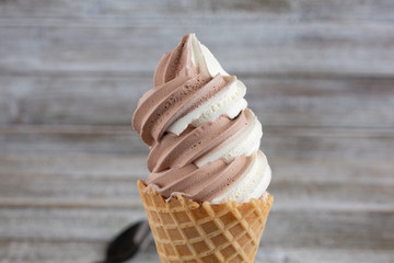 A closeup view of a frozen yogurt chocolate vanilla swirl on a waffle cone, in a restaurant or kitchen setting.