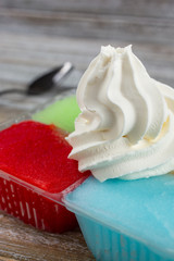 A view of a plastic container of Italian ice flavors, topped with a dollop of frozen yogurt, in a restaurant or kitchen setting.
