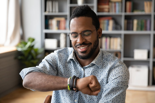 Smiling african American man in glasses look at using modern smartwatch gadget or device, happy biracial male or businessman check time on hand watch at workplace, time management concept
