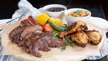 A view of a meat platter, featuring steak, sausage, and chicken, in a restaurant or kitchen setting.
