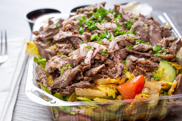 A view of a plastic container of beef shawarma salad, in a restaurant or kitchen setting.