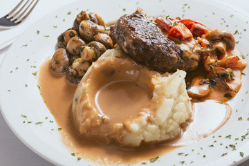 A closeup view of a plate of meatloaf with a side of mashed potatoes and gravy, in a restaurant or kitchen setting.