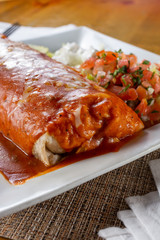 A closeup view of a wet burrito plate, in a restaurant or kitchen setting.