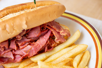 A closeup view of a pastrami sandwich and french fries, in a restaurant or kitchen setting.
