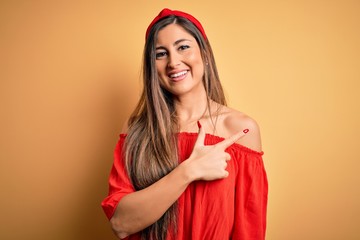 Young beautiful woman colorful summer style over yellow isolated background cheerful with a smile on face pointing with hand and finger up to the side with happy and natural expression