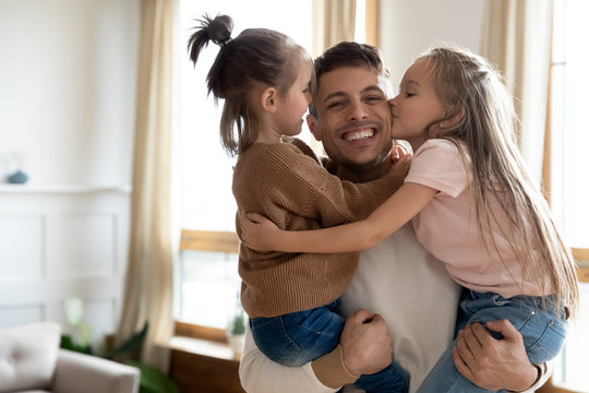 Head shot portrait of cheerful daddy holding adorable little children siblings, looking at camera. Cute small kids sisters kissing cuddling young excited father, enjoying weekend tender time together.